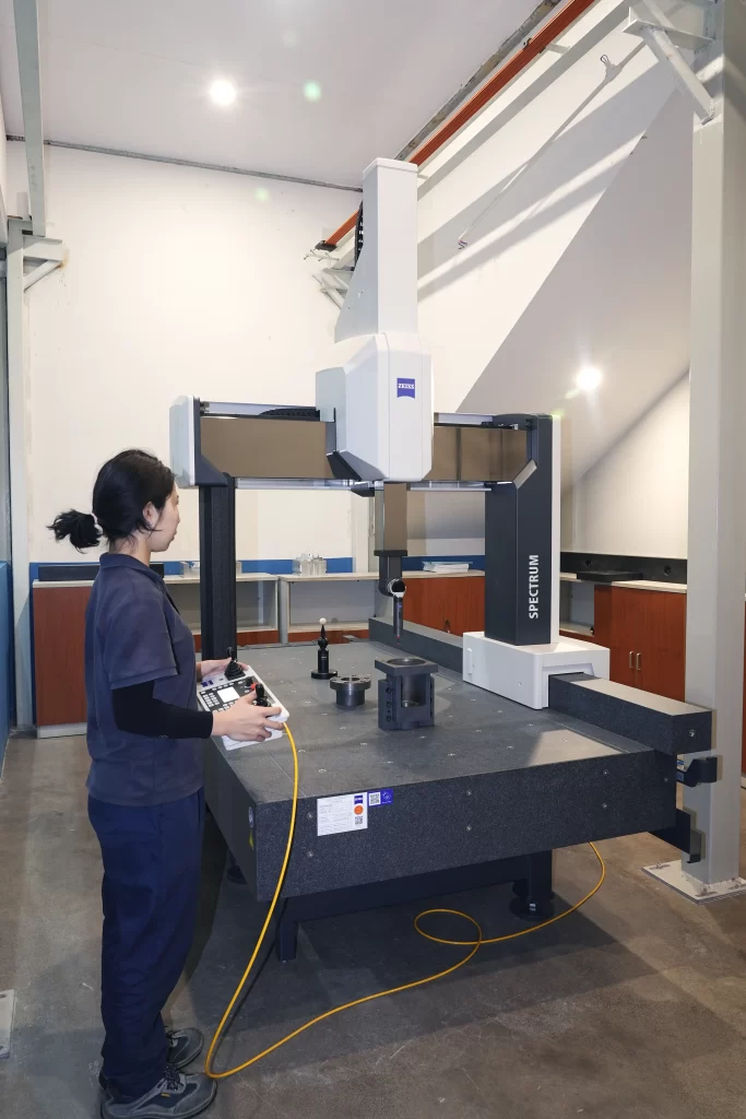 Worker operating a ZEISS Spectrum coordinate measuring machine (CMM) for precision quality inspection of CNC machined parts in a laboratory