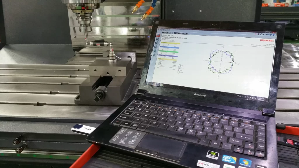  A close-up of a CNC machining center on a factory floor, with a laptop displaying Renishaw measurement software. The setup includes a precision probe and fixtures, showcasing advanced metrology for quality control in manufacturing.