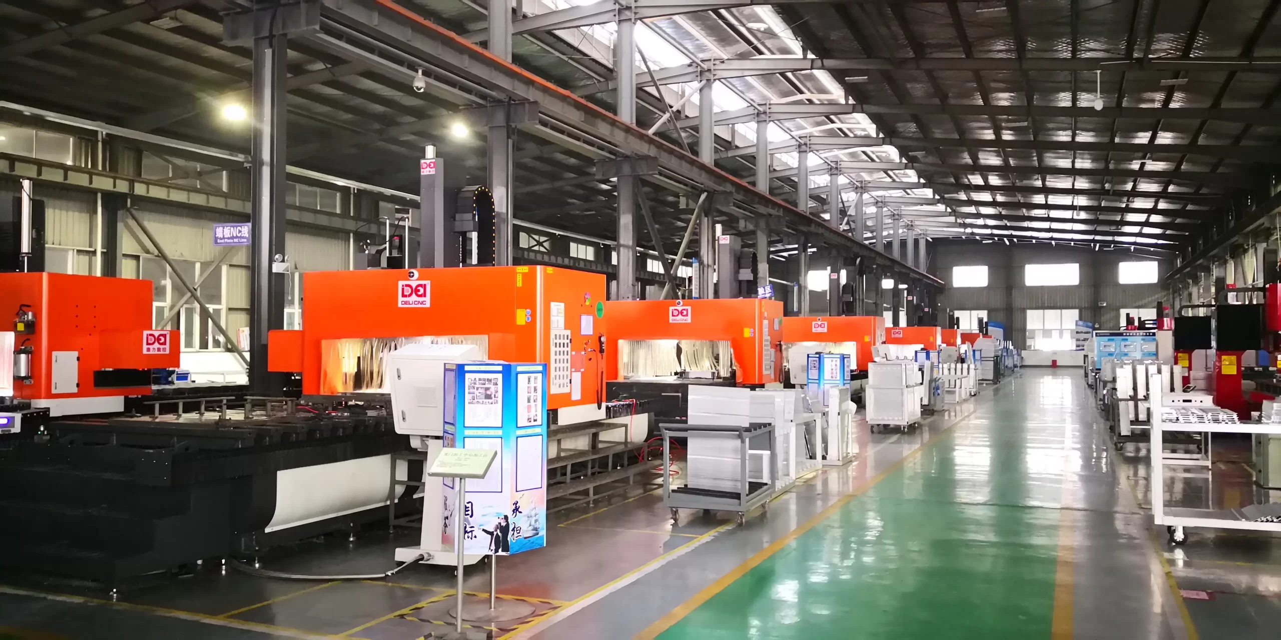 A spacious CNC machining workshop with rows of orange CNC machines, organized workstations, and a clean, well - lit industrial environment
