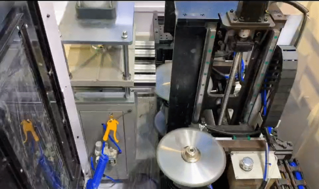 This is a close-up of the internal structure of a five-axis CNC face milling machine, showing the silver metal spindle, blue hydraulic lines, yellow manual control valve, and transparent protective cover. The core area of the machine houses a circular machining table, surrounded by precision guide rails and transmission components, creating a visual experience of the mechanical precision and automated machining of industrial-grade CNC equipment.