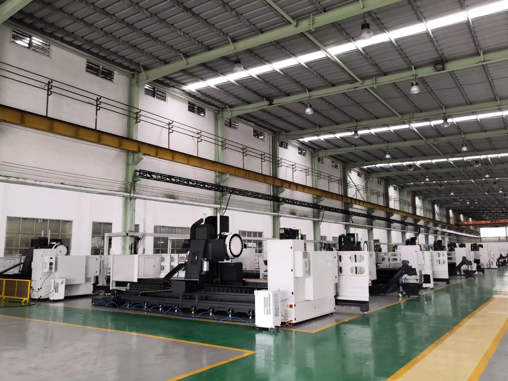 A spacious industrial workshop with neatly arranged large CNC machining centers. The green floor contrasts with white machines, while overhead cranes and LED lighting create an efficient production environment.