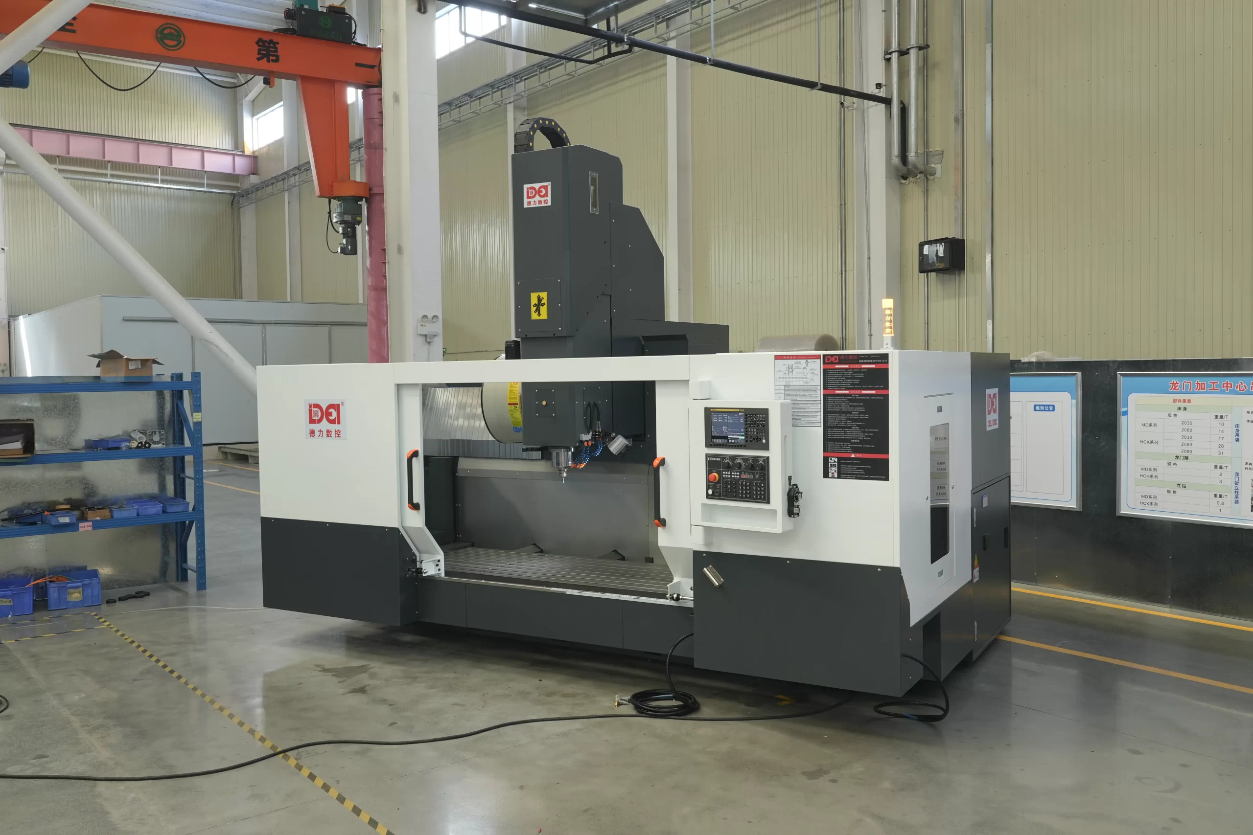 A large vertical machining center in a factory. It has a white - gray body, a red warning light, and blue racks/equipment in the background.