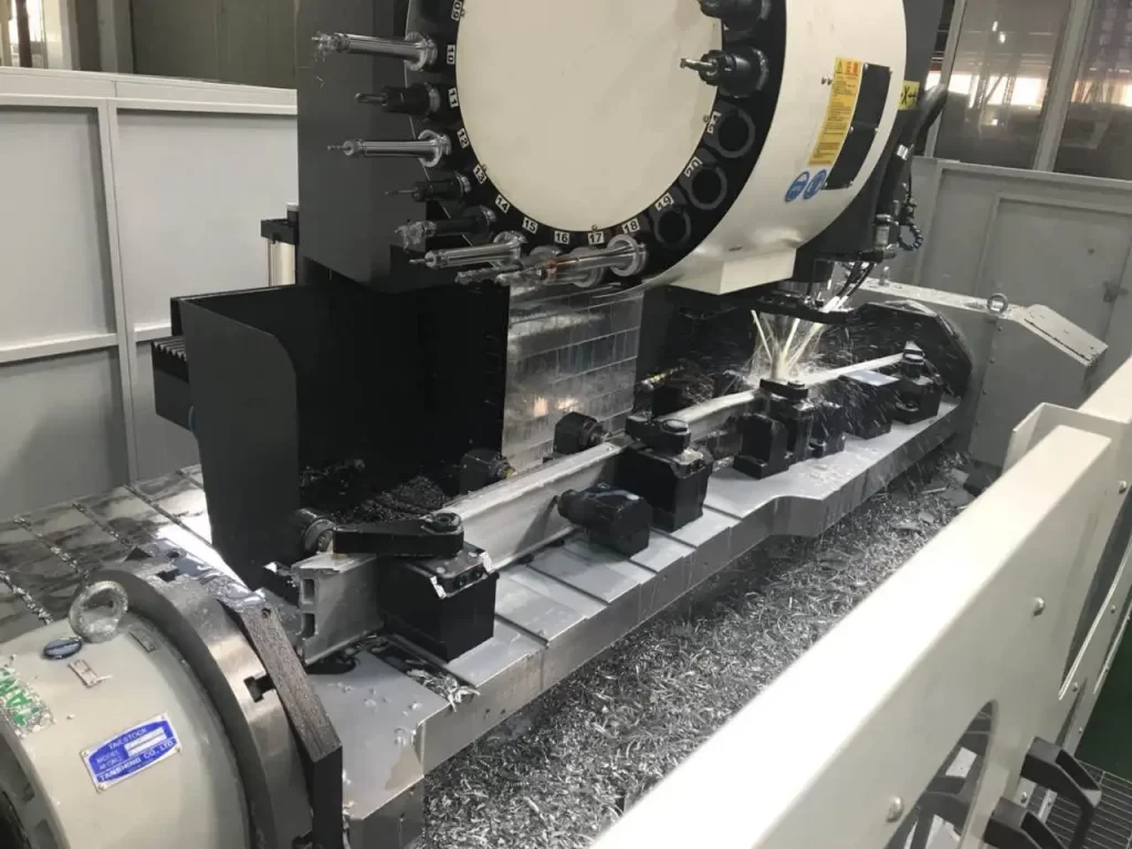 A CNC machining center in operation, with cutting tools actively processing a workpiece, coolant being sprayed, and chips scattered around.