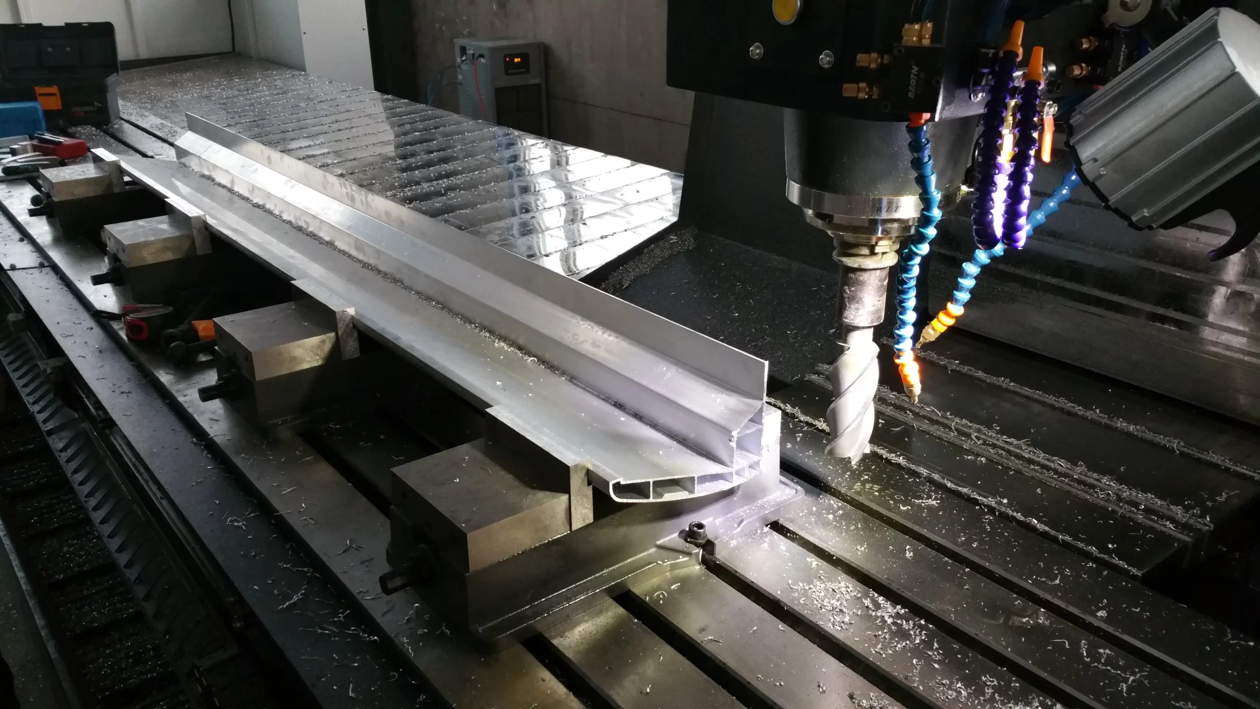 A CNC milling machine cuts a large metal component, with cutting fluid hoses and metal shavings visible, showcasing high-precision machining.