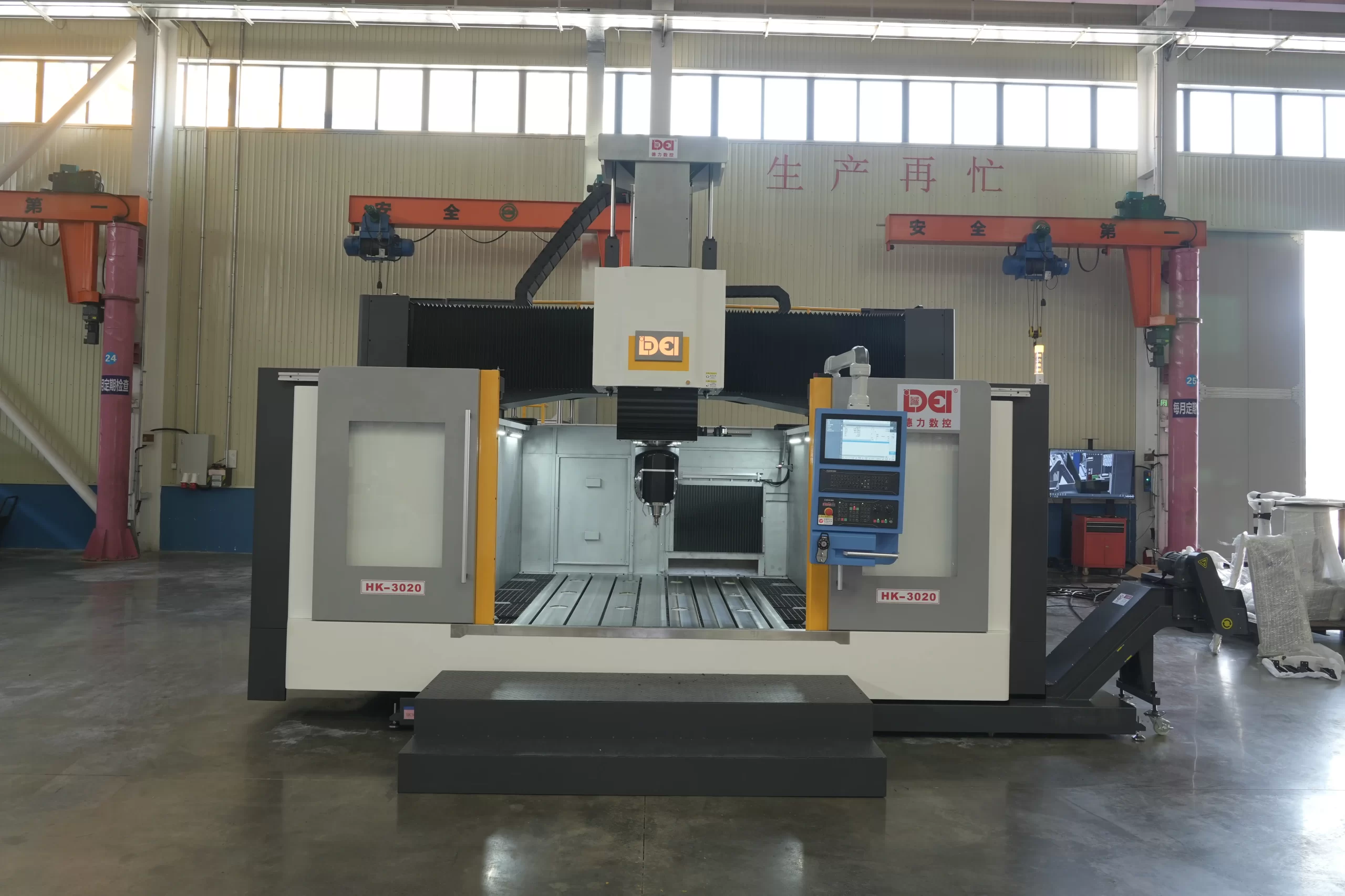 A large gantry-type CNC machining center in an industrial factory setting, with a spacious work area and control panel.
