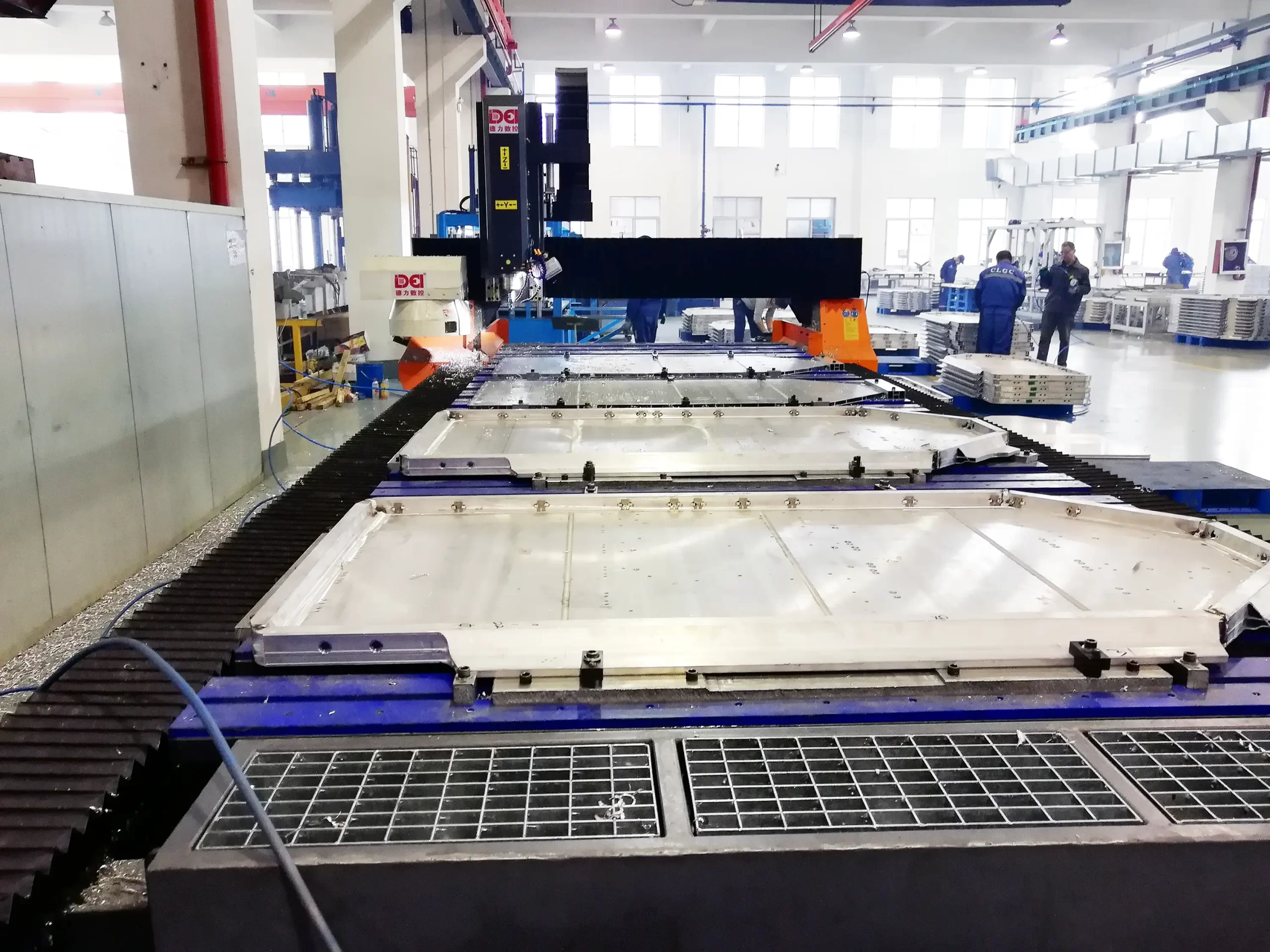 A large CNC machine processes metal components in a spacious manufacturing plant, with engineers in the background, showcasing precision machining in industrial production.