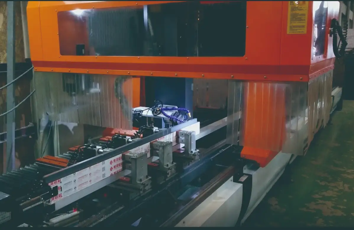 An orange vertical machining center (VMC) with transparent enclosures operates in a manufacturing workshop, with mechanical components and wiring visible inside.